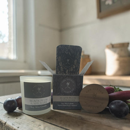 Candle and packaging with 'Black Plum & Rhubarb' branding on a wooden surface.