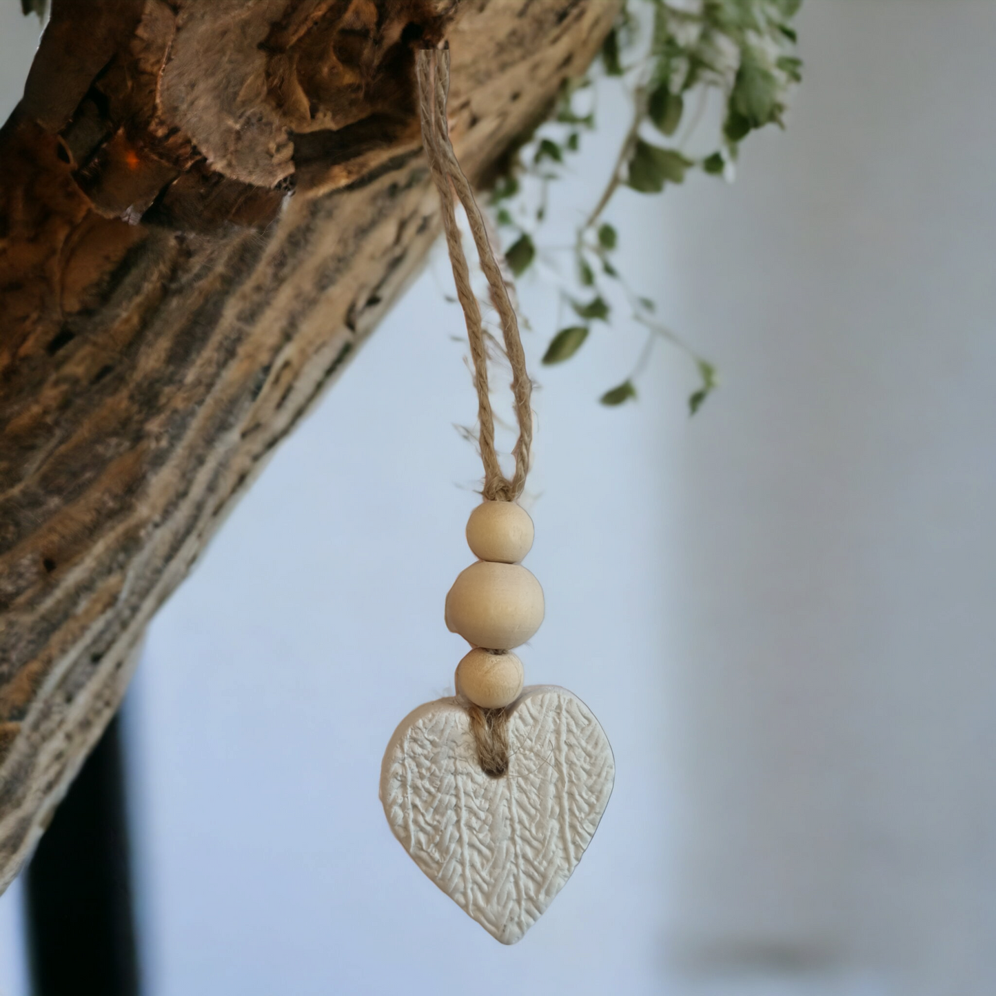 A cream clay heart-shaped air freshener hanging from a string, with a textured background.