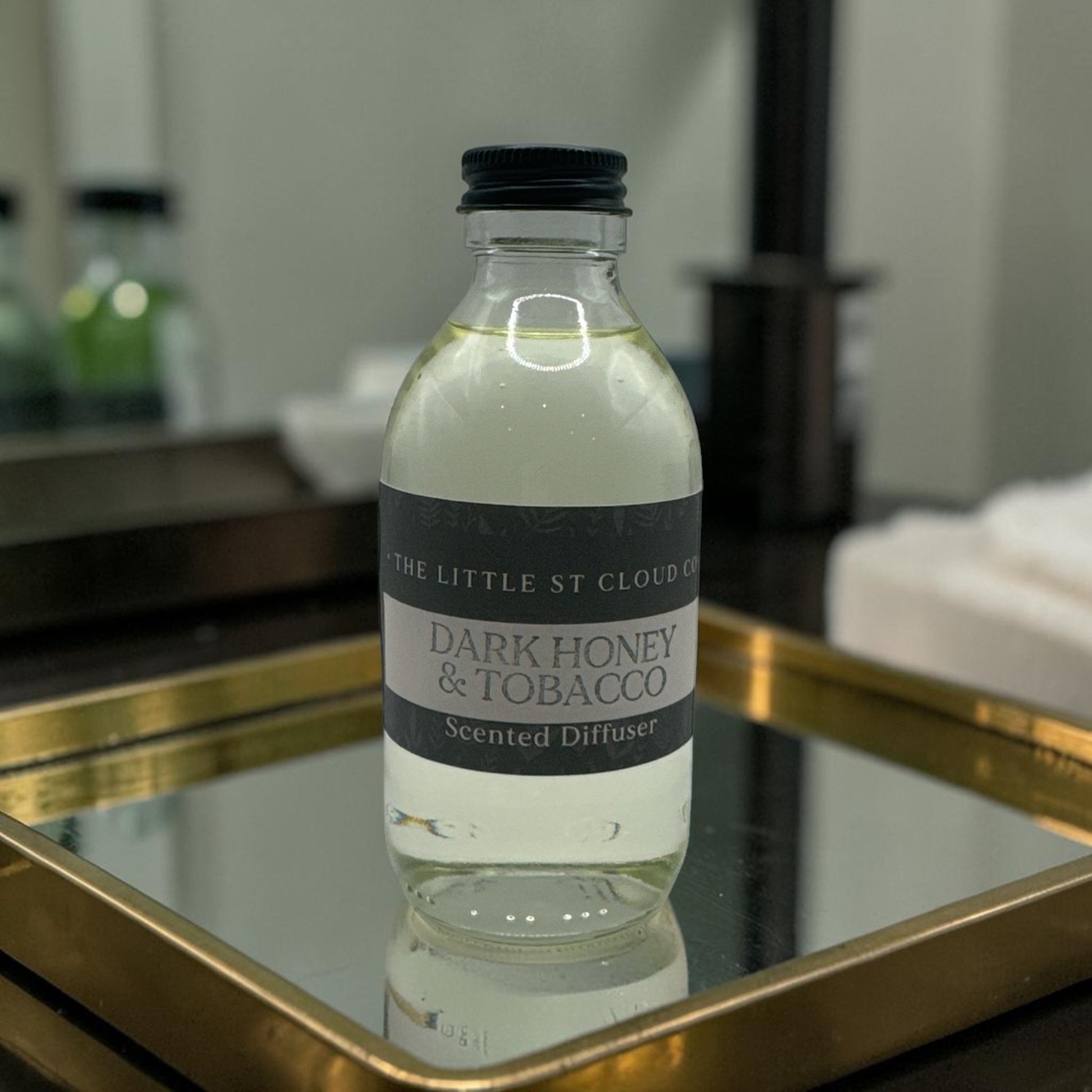Bottle of 'Dark Honey & Tobacco' scented diffuser on a mirror with a blurred background