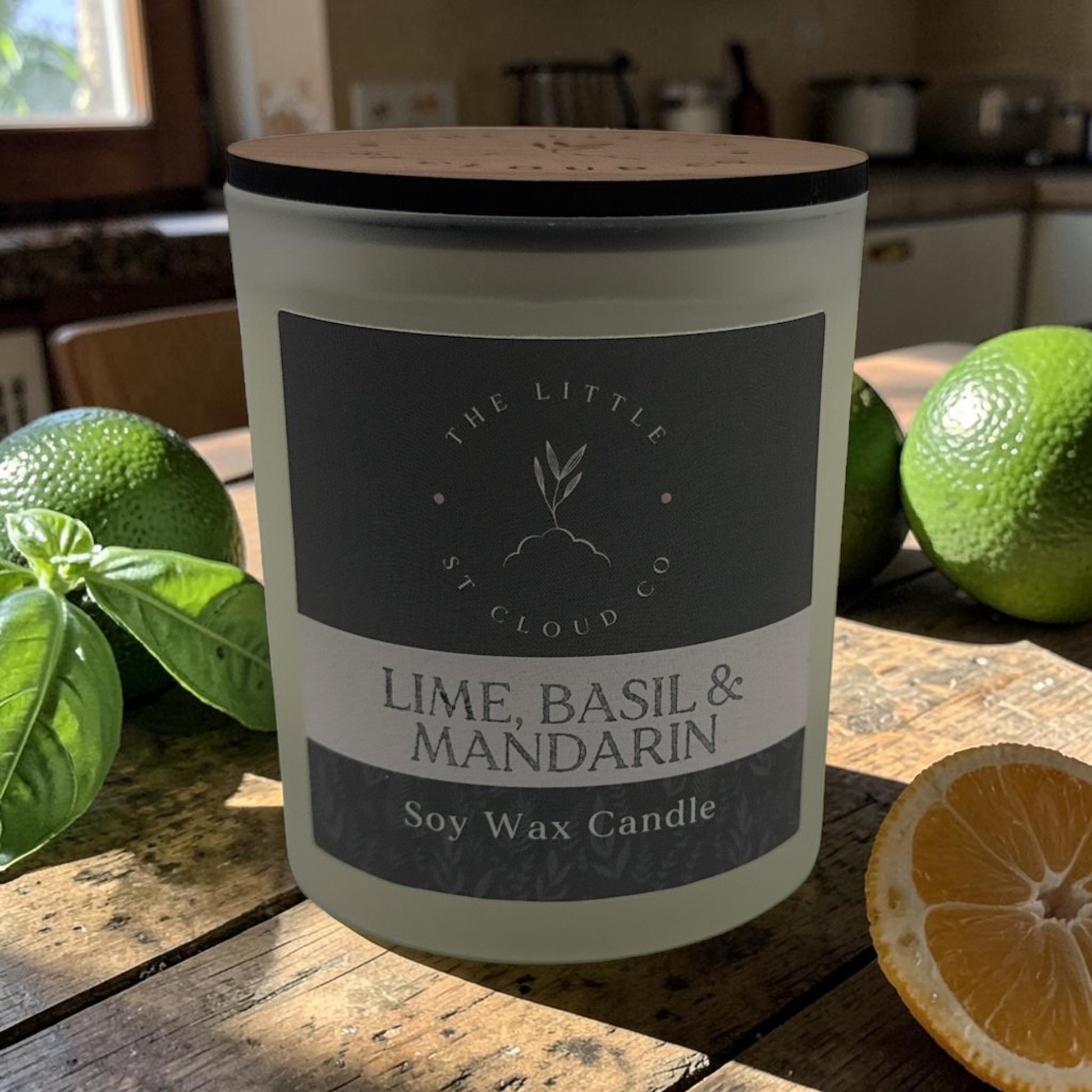 Soy wax candle labelled 'Lime, Basil & Mandarin' on a wooden surface with limes and a mandarin.