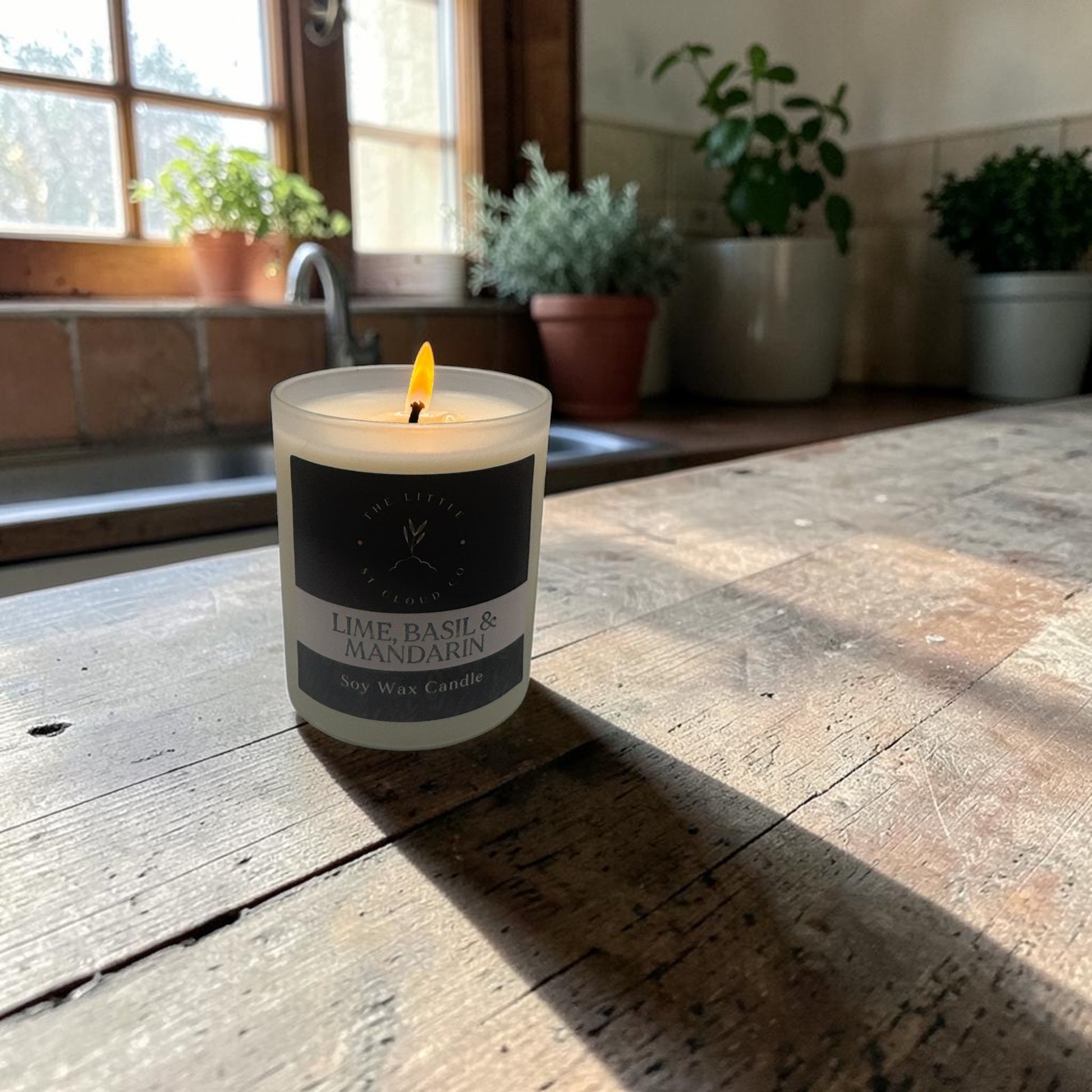 Candle with a label on a wooden surface, with plants in the background
