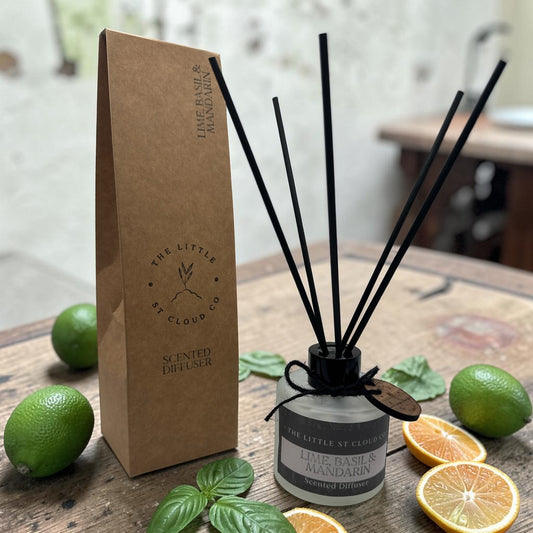 Scented diffuser with black sticks and a cardboard packaging on a wooden surface with limes and oranges.