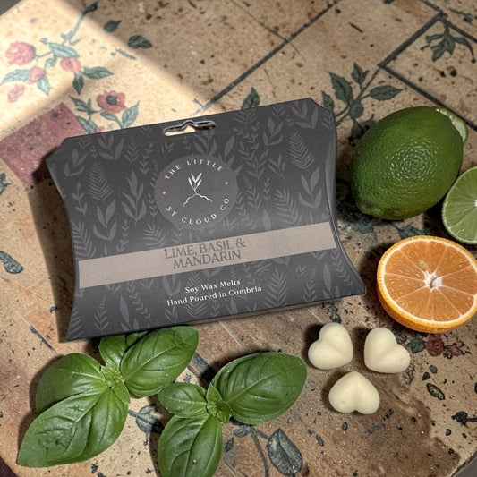 Packaged lime, basil, and mandarin wax melts on a decorative surface with fresh basil leaves and an orange.