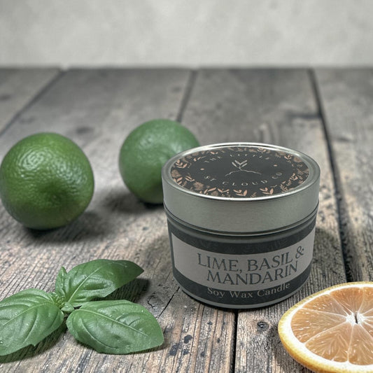 Candle labeled 'Lime, Basil & Mandarin' on a wooden surface with limes and basil leaves.