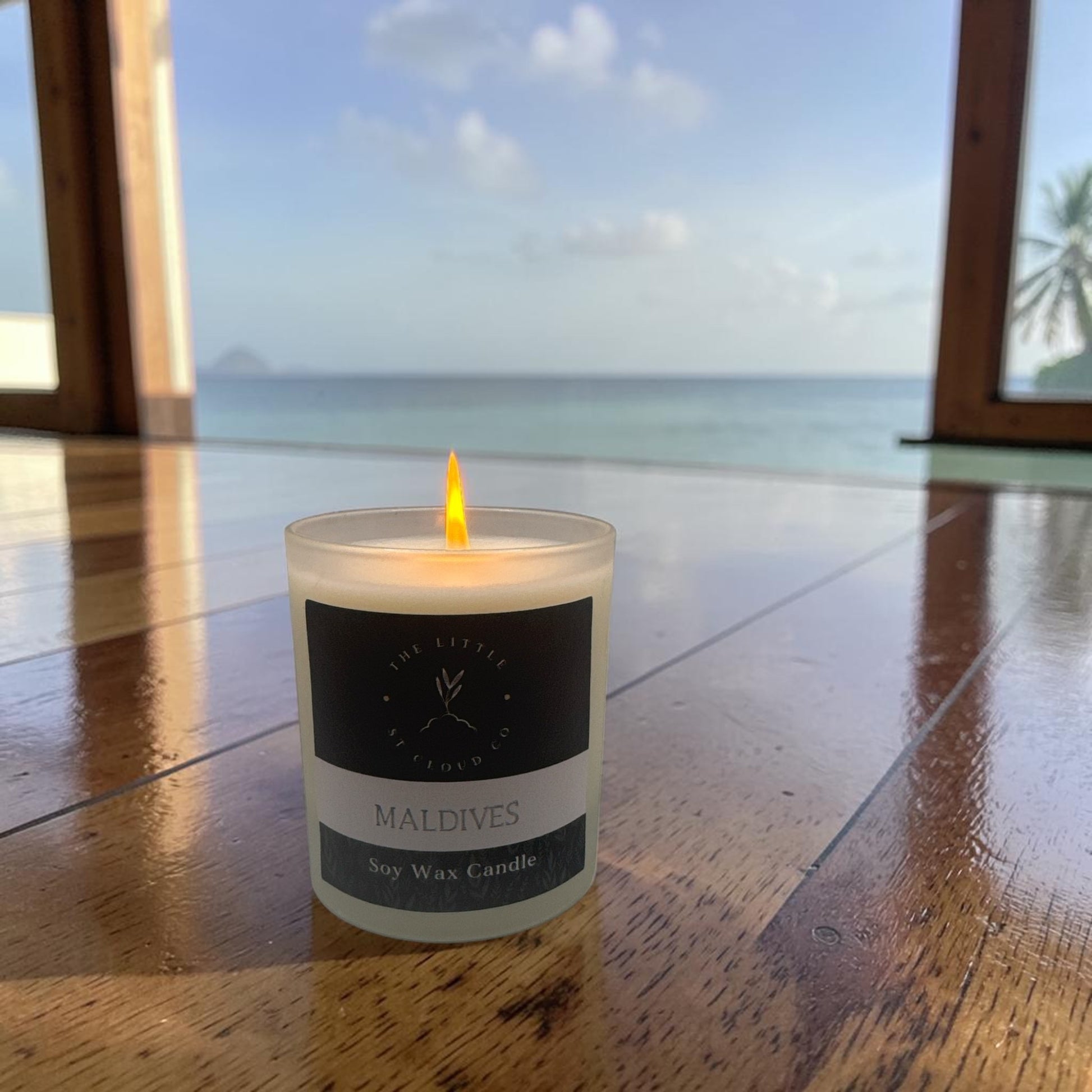 Candle labeled 'Maldives' on a wooden surface with a scenic background