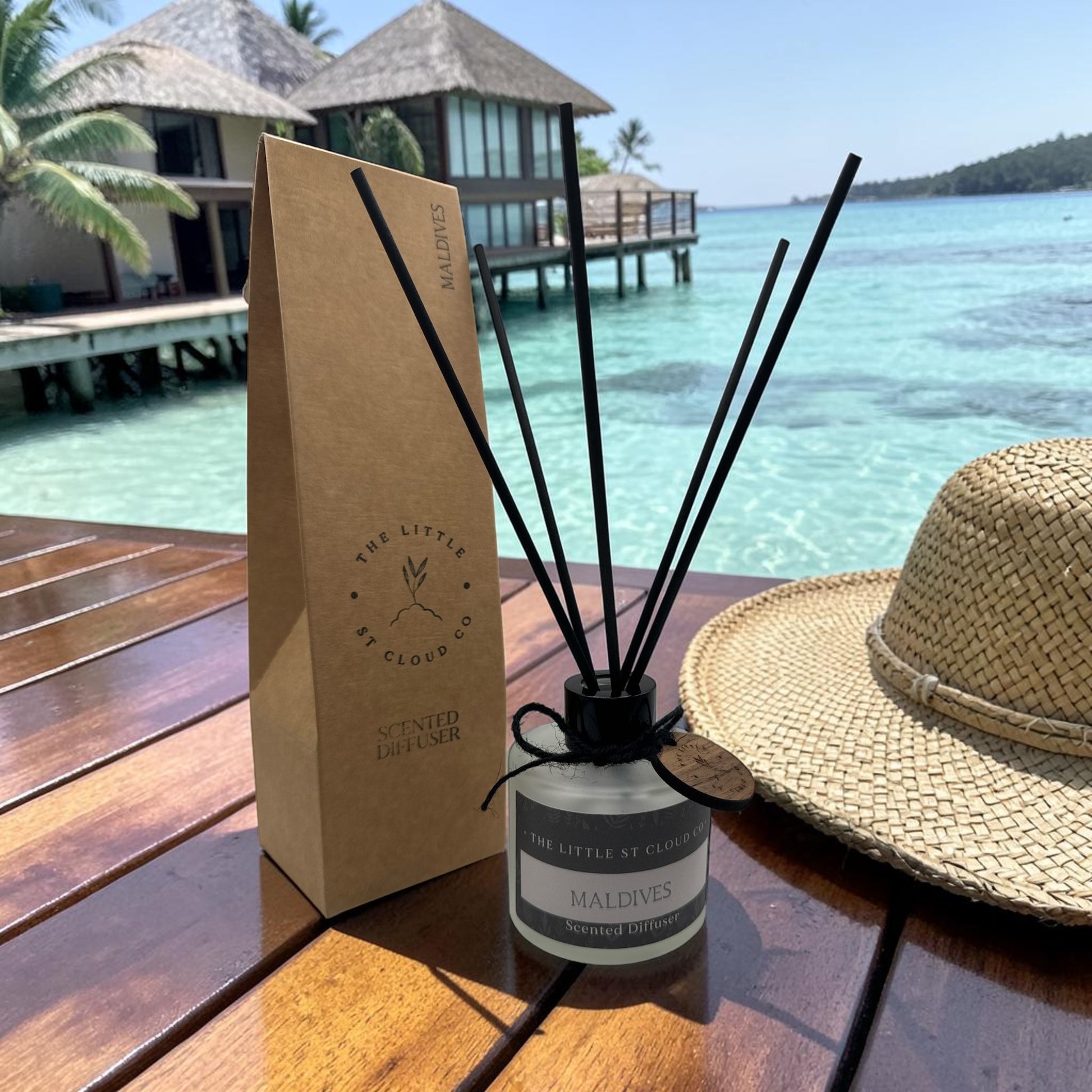 Diffuser with packaging and straw hat on a wooden table by a tropical resort.