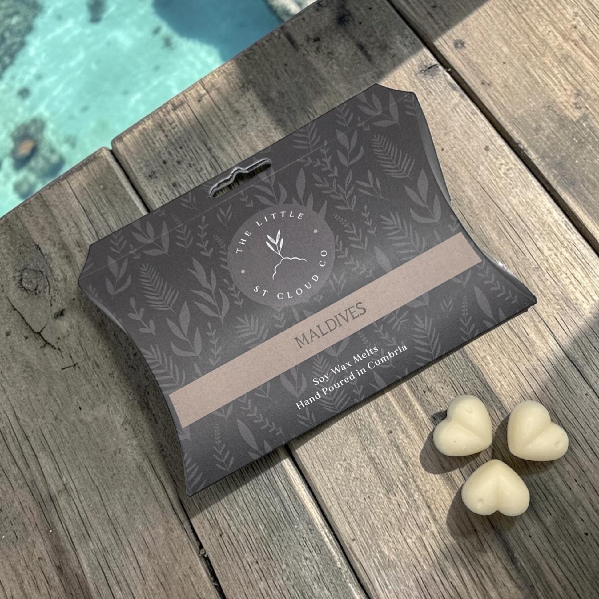 Packaged product with 'The Little St. Cloud Co' branding on a wooden surface near the tropical sea.