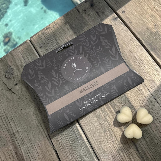 Packaged product with 'The Little St. Cloud Co' branding on a wooden surface near the tropical sea.