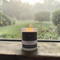 Candle labeled 'Morning Dew' on a windowsill with a garden view