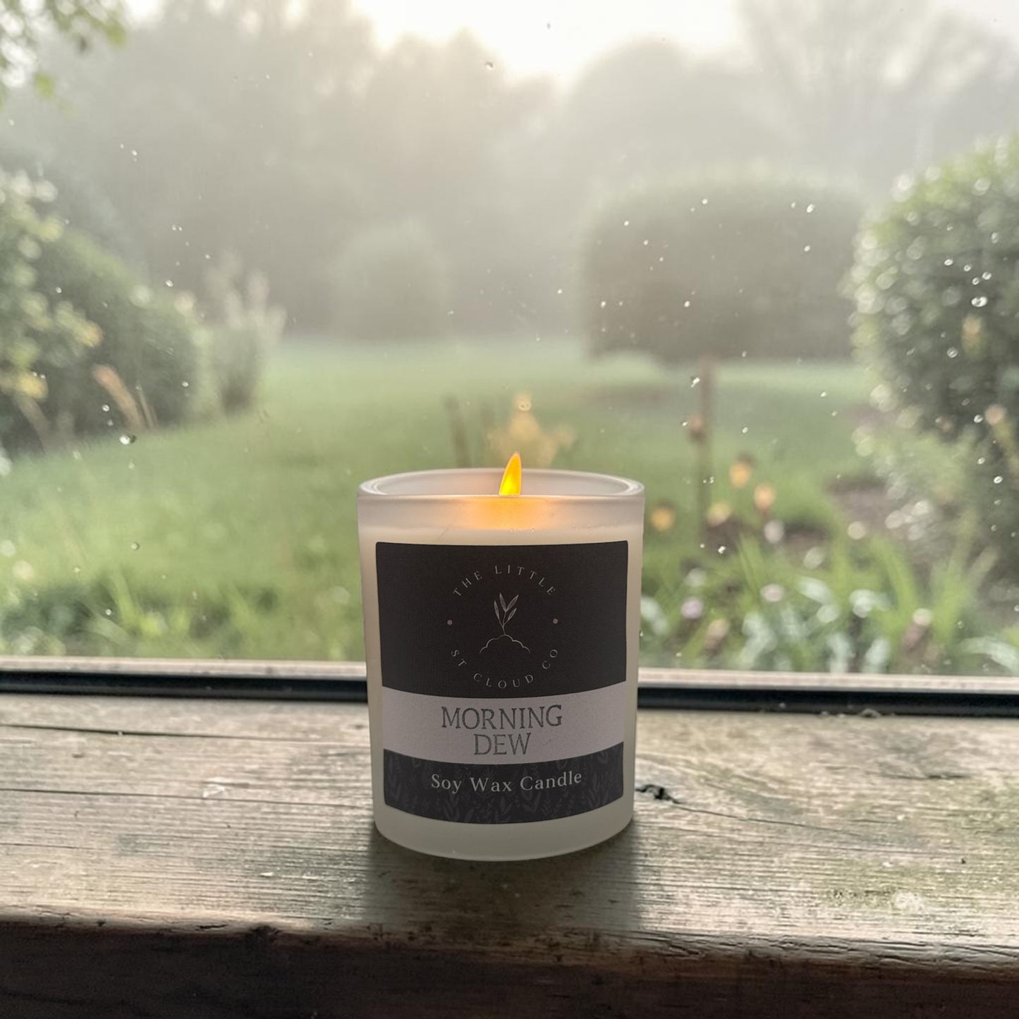 Candle labeled 'Morning Dew' on a windowsill with a garden view