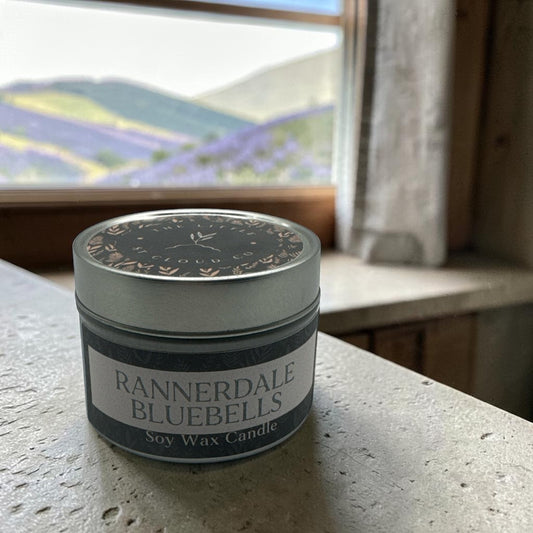 A small silver candle tin in the scent rannerdale bluebells by the little st cloud company on a countertop with views of fells and bluebells