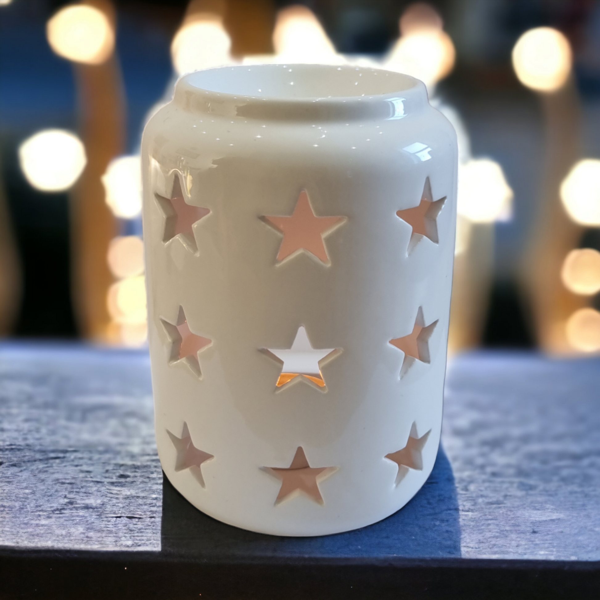 A Lit Star wax burner on a wooden table with fairy lights in the background