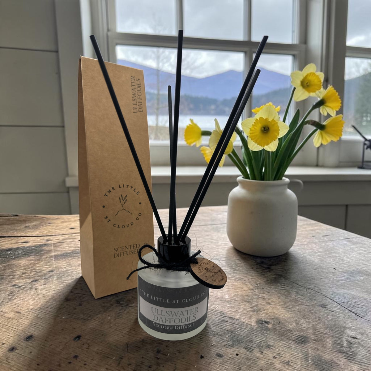Ullswater daffodil scented reed diffuser with frosted glass and black reeds by the little st cloud co with a lakeside view with a vase of daffodils