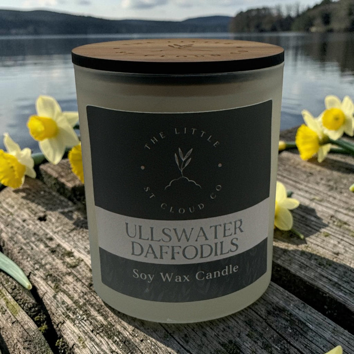 A frosted candle jar with wooden lid scented Ullswater Daffodils by the little st cloud co with a lakeside view with daffodils
