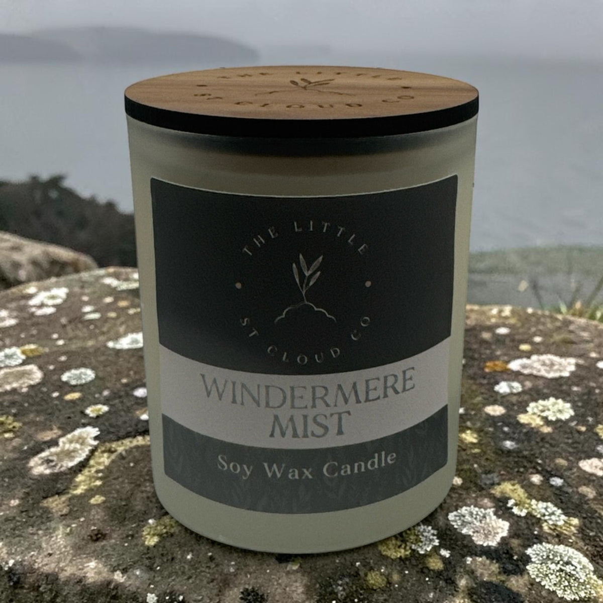 A frosted candle jar by the little st cloud co in the scent windermere mist sat on a stone wall with misty lake views