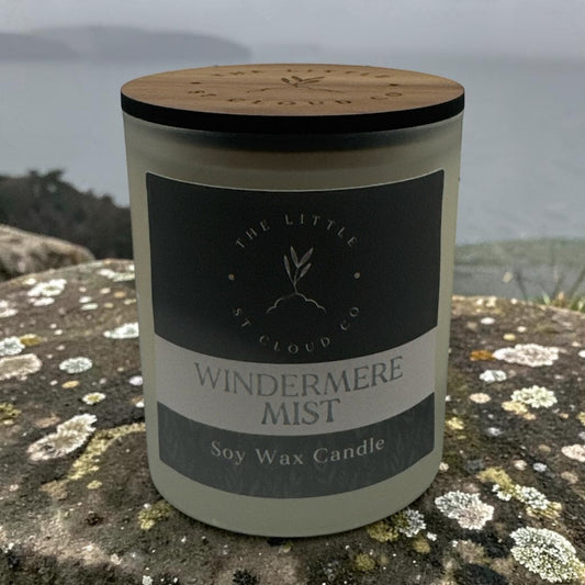 A frosted candle jar by the little st cloud co in the scent windermere mist sat on a stone wall with misty lake views